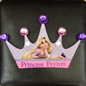 K&ouml;nnte beinhalten: Eine lila und rosafarbene Krone mit Glitzer-Finish und Strasssteinen. Die Krone zeigt ein Bild von Rapunzel aus dem Disney-Film Rapunzel - Neu verf&ouml;hnt. Die Krone tr&auml;gt den Text "Princess Peyton" auf der Vorderseite.