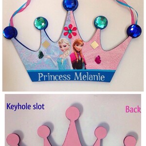 K&ouml;nnte beinhalten: Rosa Holz-Prinzessinnenkrone mit einem Schl&uuml;sselloch auf der R&uuml;ckseite. Die Vorderseite der Krone ist mit einem blauen und rosa Band, einem Bild von Elsa und Anna aus Frozen und den Worten "Princess Melanie" verziert.