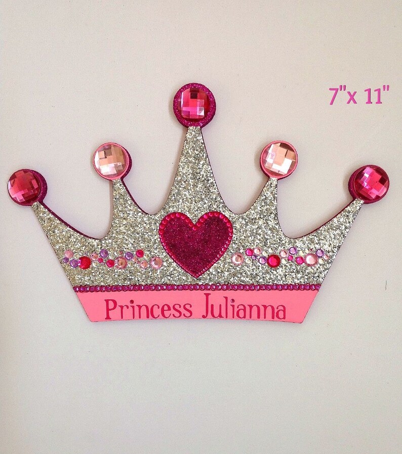 K&ouml;nnte beinhalten: Eine silberne Glitzer-Prinzessinnenkrone mit rosa Akzenten und Strasssteinen. Die Krone hat ein pinkfarbenes Herz in der Mitte und die Worte "Princess Julianna" unten. Die Krone ist 17,8 cm x 27,9 cm gro&szlig;.