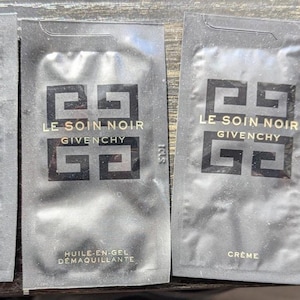 Op de afbeelding: Vier zwarte Givenchy huidverzorgingsproductmonsters. Drie zijn zakjes met het label "LE SOIN NOIR" met "SERUM", "HUILE-EN-GEL DEMAQUILLANTE" en "CREME". Een klein doosje "CREME" is ook inbegrepen.