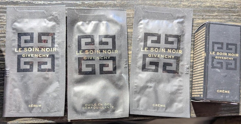 Op de afbeelding: Vier zwarte Givenchy huidverzorgingsproductmonsters. Drie zijn zakjes met het label "LE SOIN NOIR" met "SERUM", "HUILE-EN-GEL DEMAQUILLANTE" en "CREME". Een klein doosje "CREME" is ook inbegrepen.