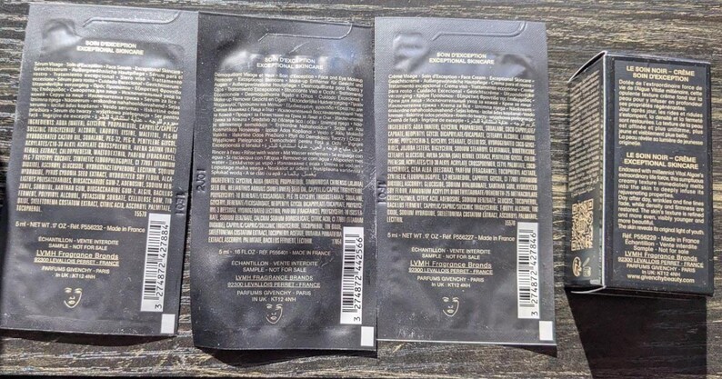Op de afbeelding: Vier zwarte samplezakjes en een kleine zwarte doos worden getoond. De zakjes en de doos hebben witte tekst en een logo. De zakjes zijn gelabeld met "BON D'EXEPTION EXCEPTIONAL SKINCARE". De doos is gelabeld met "LE BON NOIR - CR&Egrave;ME BOIS D'EXEPTION".