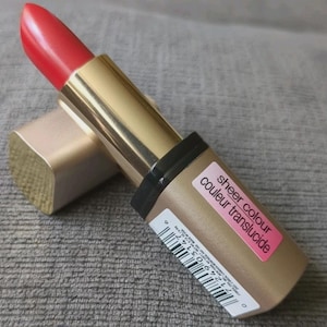 May include: A red lipstick with a gold-colored tube and a black band. The lipstick is open, revealing the red color. The label on the lipstick reads "sheer colour couleur translucide".