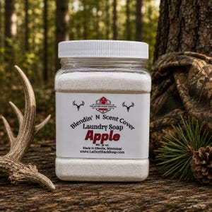 Puede incluir: Un recipiente cuadrado de pl&aacute;stico transparente lleno de detergente en polvo blanco. La etiqueta dice Blendin' N Scent Cover Laundry Soap Apple, Wt. 32 oz., Made in Ellisville, Mississippi, y www.LatherShackSoap.com, con un logo de granero rojo y astas de ciervo.