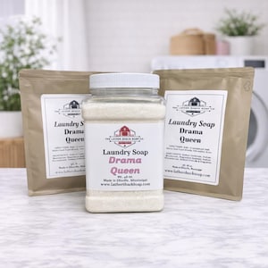 May include: A clear plastic jar and two brown paper bags of laundry soap. The jar has a white lid and a label that reads "Laundry Soap Drama Queen." The bags also have labels with the same text and a barn logo.