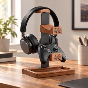 May include: A black metal and brown wood gaming stand featuring a rectangular base, a vertical support, and two horizontal arms. The wood arms are engraved with a large letter K and the name Kandace. Black headphones and a black game controller rest on the stand.