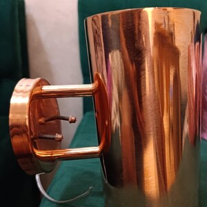 May include: A copper-colored wall sconce with a cylindrical shade and a bracket for mounting. The sconce has a polished finish, reflecting the light. The fixture is designed for indoor use and adds a touch of elegance to any room.