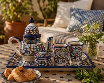 Może przedstawiać: Ceramiczny zestaw do herbaty z imbrykiem, cukiernicą i dwoma filiżankami, wszystkie z białą podstawą i skomplikowanymi niebieskimi, żółtymi i czerwonymi wzorami. Zestaw stoi na pasującej tacy, obok miski z ciastkami. Przytulna atmosfera.