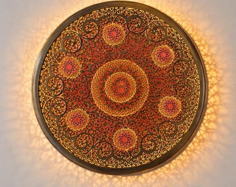 May include: A round, decorative wall hanging with an intricate, laser-cut design. The piece features a dark brown frame and a red and gold patterned interior with a central medallion and radiating floral motifs.