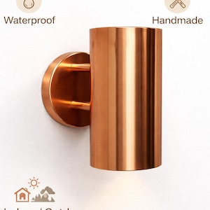 May include: A copper-coloured cylindrical wall sconce with a circular base and two small support arms. The sconce is labelled "Waterproof", "Handmade", and "Indoor / Outdoor".
