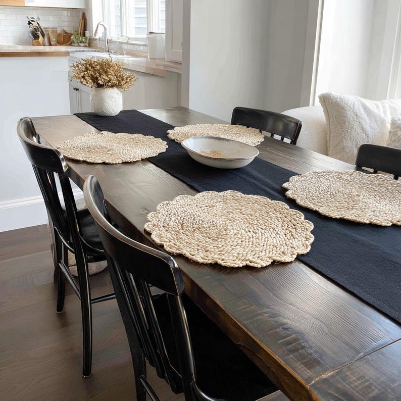 K&ouml;nnte beinhalten: Ein rustikaler Esstisch, gedeckt f&uuml;r eine Mahlzeit. Der dunkle Holztisch ist mit einem schwarzen Tischl&auml;ufer, gewebten Platzsets und einer Keramikschale geschm&uuml;ckt. Schwarze St&uuml;hle umgeben den Tisch.