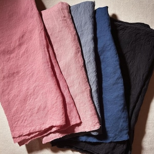May include: A selection of folded linen napkins in a range of colours, including pink, blue, and black. The napkins have a textured appearance and a soft, natural look. The arrangement showcases the different hues and the fabric's subtle variations.