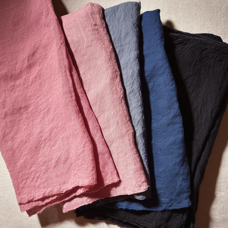 May include: A selection of folded linen napkins in a range of colours, including pink, blue, and black. The napkins have a textured appearance and a soft, natural look. The arrangement showcases the different hues and the fabric's subtle variations.