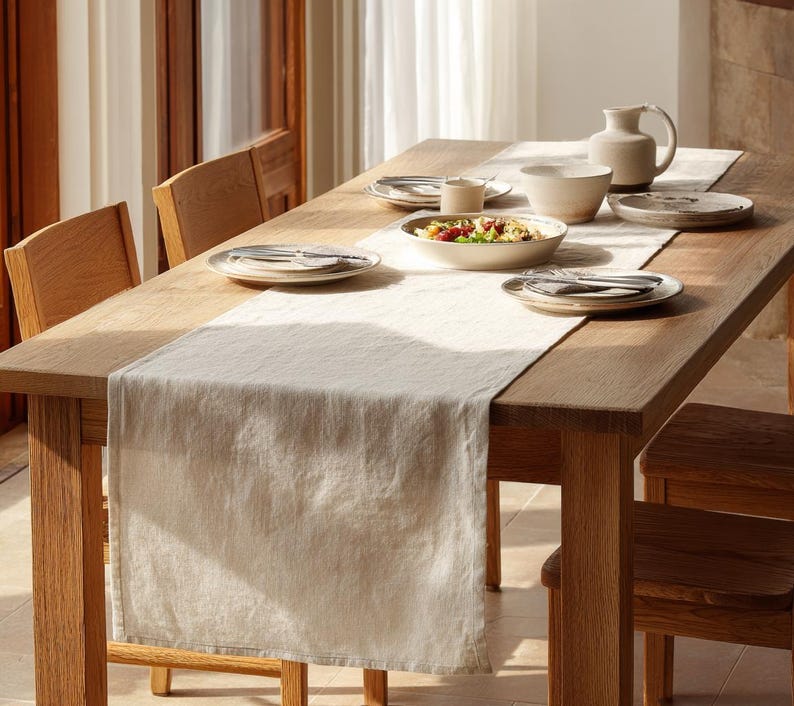 K&ouml;nnte beinhalten: Ein Holztisch, der f&uuml;r eine Mahlzeit gedeckt ist. Der Tisch ist aus hellbraunem Holz und hat einen cremefarbenen Tischl&auml;ufer. Der Tisch ist mit Tellern, Sch&uuml;sseln, Besteck und einem Krug gedeckt. Ein Salat befindet sich in einer Sch&uuml;ssel.