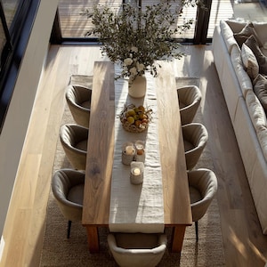 Op de afbeelding: Een bovenaanzicht van een eetkamer met een grote houten tafel. De tafel is versierd met een neutrale loper, een fruitmand, kaarsen en een vaas met bloemen. Acht gestoffeerde stoelen omringen de tafel.