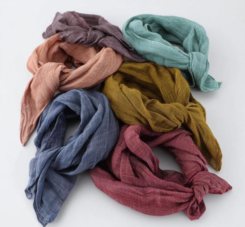 K&ouml;nnte beinhalten: Sieben geknotete Schals in verschiedenen Farben, darunter Staubrosa, T&uuml;rkis, Senfgelb, Tiefrot, Marineblau und ged&auml;mpftes Lila. Der Stoff scheint leicht und strukturiert zu sein, geeignet f&uuml;r w&auml;rmeres Wetter.