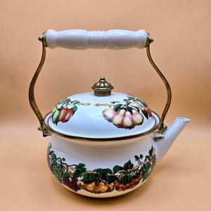 May include: White enamel teapot with a fruit design. The teapot features a white handle and spout, with gold-colored accents. The lid and body are decorated with colorful illustrations of various fruits, including pears, grapes, and apples.