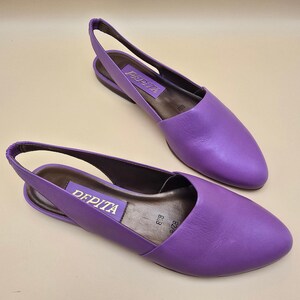 May include: A pair of purple leather slingback flats with a pointed toe and an elasticized heel strap. The interior insole is dark brown with a purple label featuring the text PAPITA in gold lettering and the size 8.5B printed on the footbed.