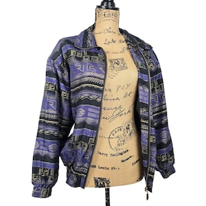 May include: A long-sleeve zip-up jacket featuring a repeating geometric pattern in shades of purple, black, and gold. The jacket has a high collar, a full-length front zipper, and elasticized cuffs at the wrists, showcasing a detailed print.
