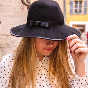 May include: A woman wearing a white shirt with black polka dots and a wide-brimmed black hat with a black ribbon.