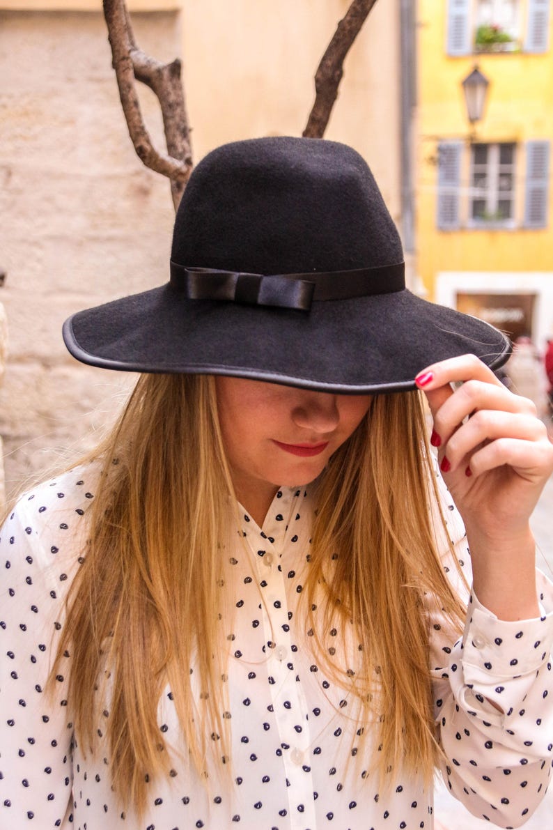 May include: A woman wearing a white shirt with black polka dots and a wide-brimmed black hat with a black ribbon.