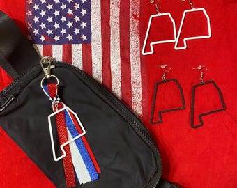 May include: A black nylon belt bag with a silver logo, featuring a keychain with a white Alabama state outline charm and red, white, and blue glitter ribbons. Two pairs of dangling earrings are included: one white and one black Alabama outline.