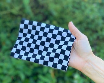 May include: A black and white checkered flag, held in a hand, against a blurred green background. The flag is made of fabric and features a classic racing or finish line pattern.