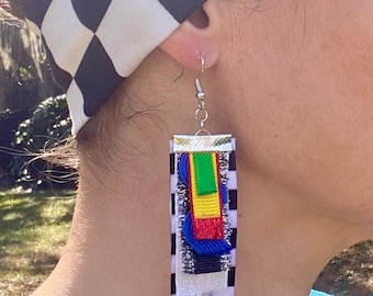 May include: Rectangular earrings with a black and white checkered pattern, accented with colorful ribbons in blue, green, yellow, and red. The earrings are suspended from silver hooks. A matching checkered headband is also visible.