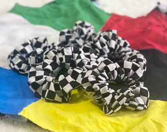 May include: A collection of black and white checkered scrunchies. The scrunchies are made of fabric and are gathered around an elastic band. The background is a colorful patchwork of fabric in various colors, including green, red, yellow, and blue.