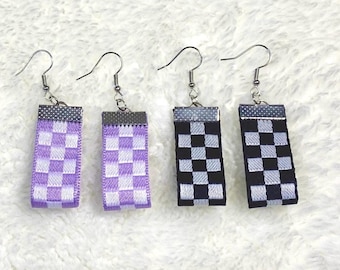 May include: Four pairs of earrings with a rectangular shape. Two pairs are purple and white checkered, and two pairs are black and white checkered. Each earring has a silver-colored hook.