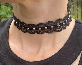 May include: Black lace choker necklace with silver-colored studs. The choker is worn around the neck and is made of delicate lace. The studs are evenly spaced along the choker's edge, adding a touch of sparkle.