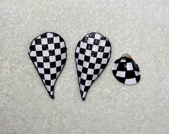 May include: Three seashells with a black and white checkered pattern. Two shells are elongated, teardrop-shaped, and the third is a smaller, round shell. The shells are arranged on a white, textured surface.