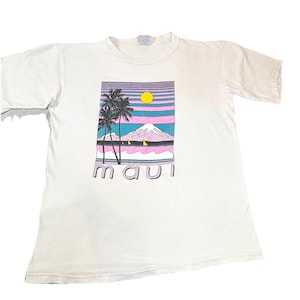 May include: White t-shirt featuring a colorful graphic of a tropical scene. The design includes palm trees, a mountain, and the word "MAUI" in a retro font. The graphic has pink, blue, yellow, and purple hues.