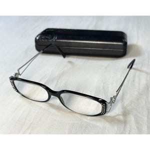 May include: Black rectangular spectacles featuring silver-tone metal temples and small clear rhinestones embedded along the outer edges of the frame front. The glasses are accompanied by a matching black rectangular hard-shell protective case.