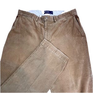 May include: Tan corduroy trousers with a button closure and pockets. The trousers have a classic fit and a Polo by Ralph Lauren label on the inside waistband. The corduroy fabric has a ribbed texture.