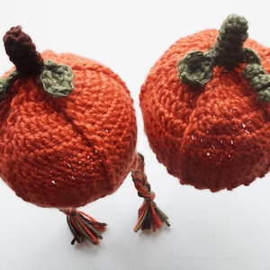 Two finished pumpkin hat pattern samples propped upright, styled to look like pumpkins with green leaf and burgundy stem toppers