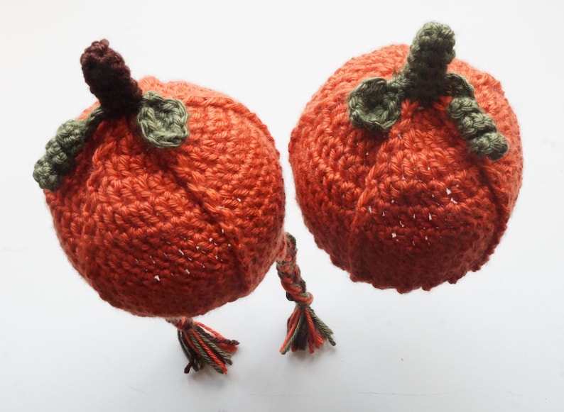 Two finished pumpkin hat pattern samples propped upright, styled to look like pumpkins with green leaf and burgundy stem toppers