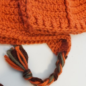 Close-up of the pumpkin hat pattern's ribbed brim and earflap, showing the braided drawstring tie with tasseled ends