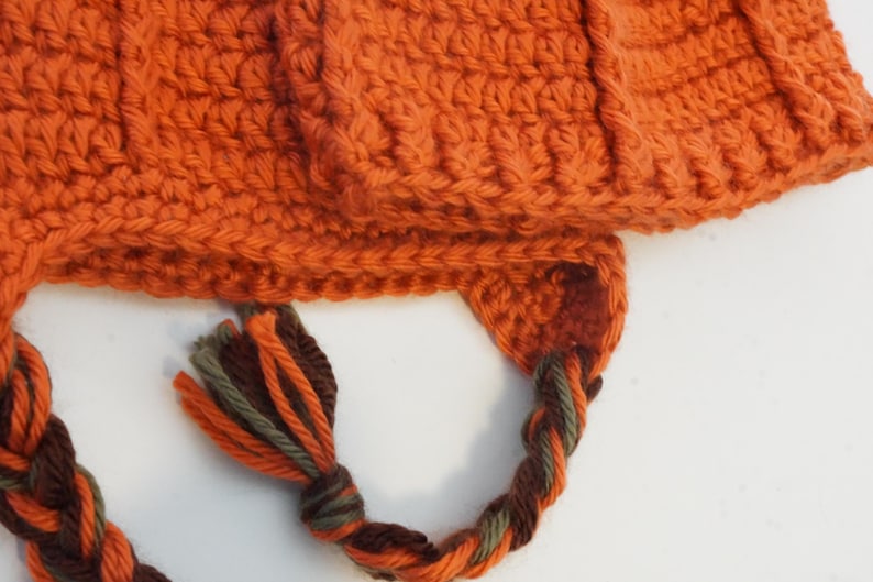 Close-up of the pumpkin hat pattern's ribbed brim and earflap, showing the braided drawstring tie with tasseled ends