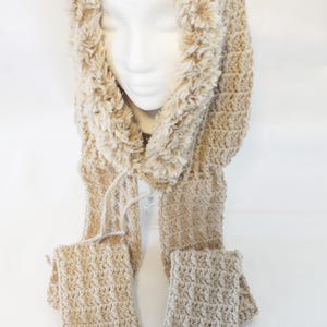 May include: A beige crocheted hood and scarf set with faux fur trim. The hood has a soft, textured appearance and is connected to a long scarf with hand warmer pockets at the ends. The scarf and hood are made of a soft, warm material.