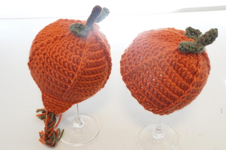 Side view of two pumpkin hat pattern samples on glass stands, highlighting the spiral ribbing and stem toppers