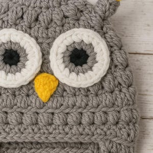 Pode incluir: Um chap&eacute;u de coruja de croch&ecirc; cinza com olhos grandes com bordas brancas e um bico amarelo. O chap&eacute;u apresenta abas para as orelhas e um tufo de fio amarelo e cinza no topo. O chap&eacute;u feito &agrave; m&atilde;o &eacute; projetado para crian&ccedil;as.