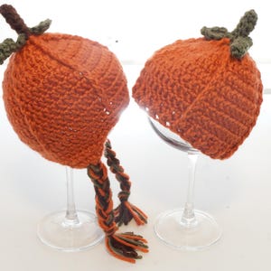 Crochet pumpkin hat pattern samples displayed upside down on glass stands, showing the ribbed pumpkin shape and dangling braided ties
