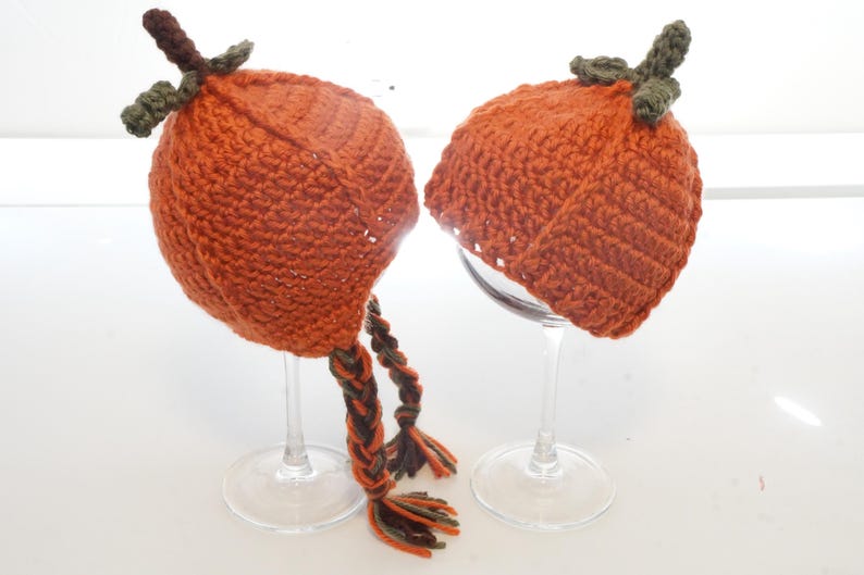 Crochet pumpkin hat pattern samples displayed upside down on glass stands, showing the ribbed pumpkin shape and dangling braided ties