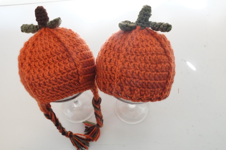 Two crochet pumpkin hat pattern samples with earflaps and braided ties, shown right-side up with leaf stem toppers on top