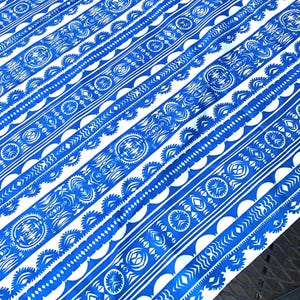 May include: A fabric textile featuring a repeating pattern of bold blue and white geometric stripes. The design includes intricate circular motifs, scalloped edges, and rows of small diamonds and chevrons arranged in a continuous diagonal layout.