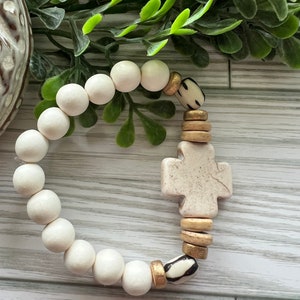 May include: White bead bracelet with a cross charm and gold and black accents.