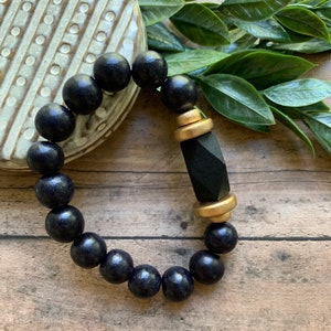 May include: A black wooden beaded bracelet with a gold and black geometric charm.