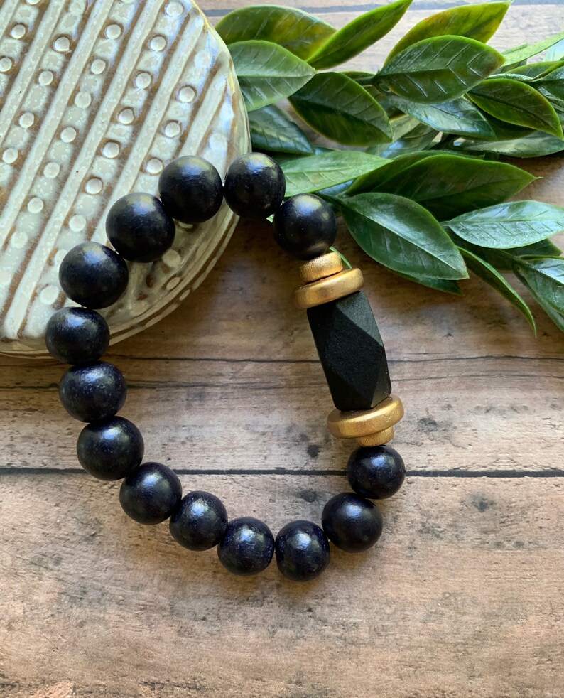 May include: A black wooden beaded bracelet with a gold and black geometric charm.