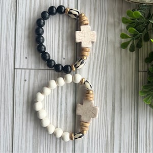 May include: Two beaded bracelets with cross charms. One bracelet is black and white, the other is white with gold accents.